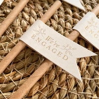 brown  cream and gold foil paper straw flags for engagement party with we're engaged on the front