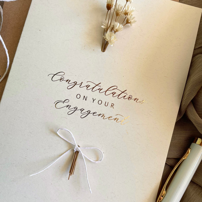 Engagement card with 'Congratulations on your Engagement' text, a white bow, and small floral arrangement.