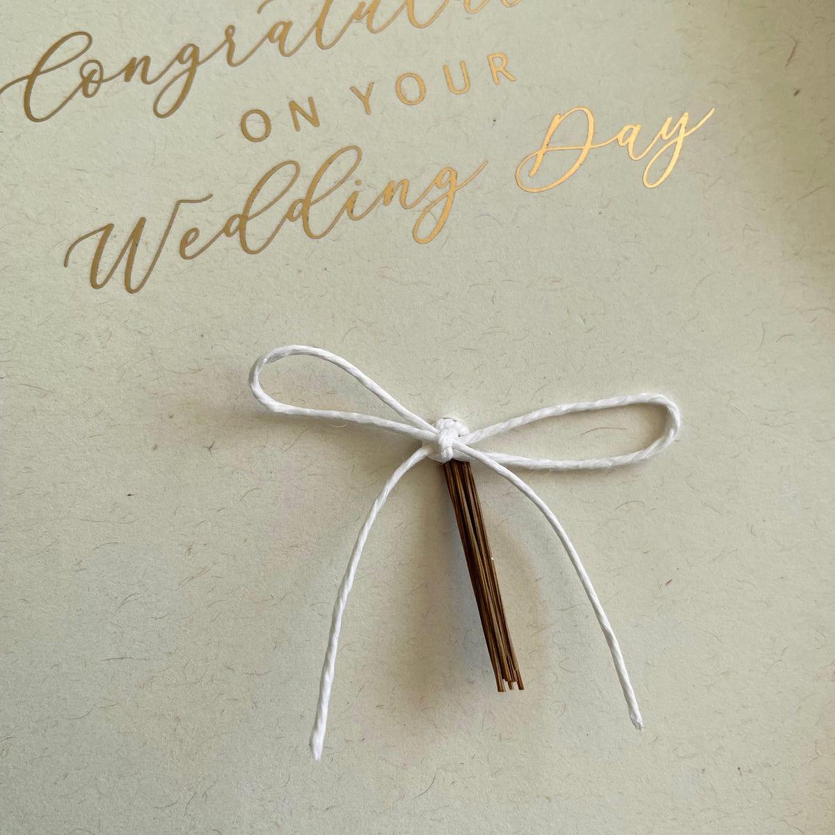 Card with 'Congratulations on your wedding day' text and a white twine bow on a ivory card and gold foil text 