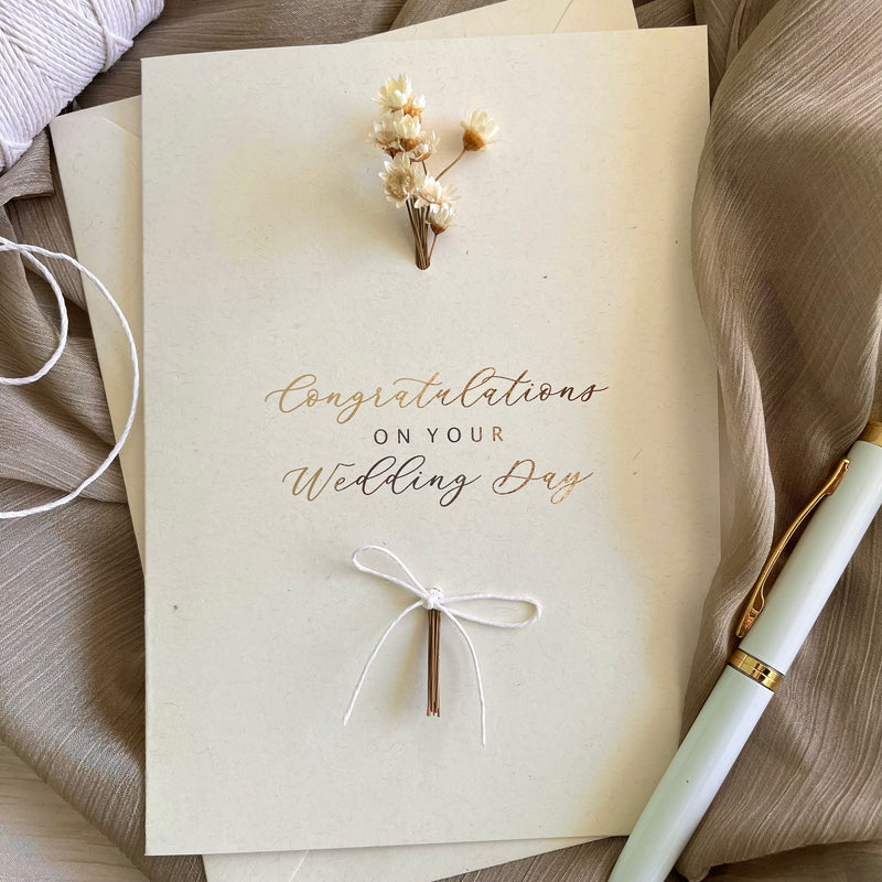 Wedding card with 'Congratulations on your wedding day'gold  text, small dried flower bouquet.