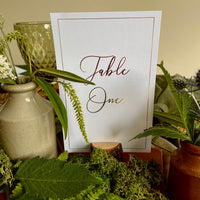 a white table number card with gold foil script and border for elegant wedding style