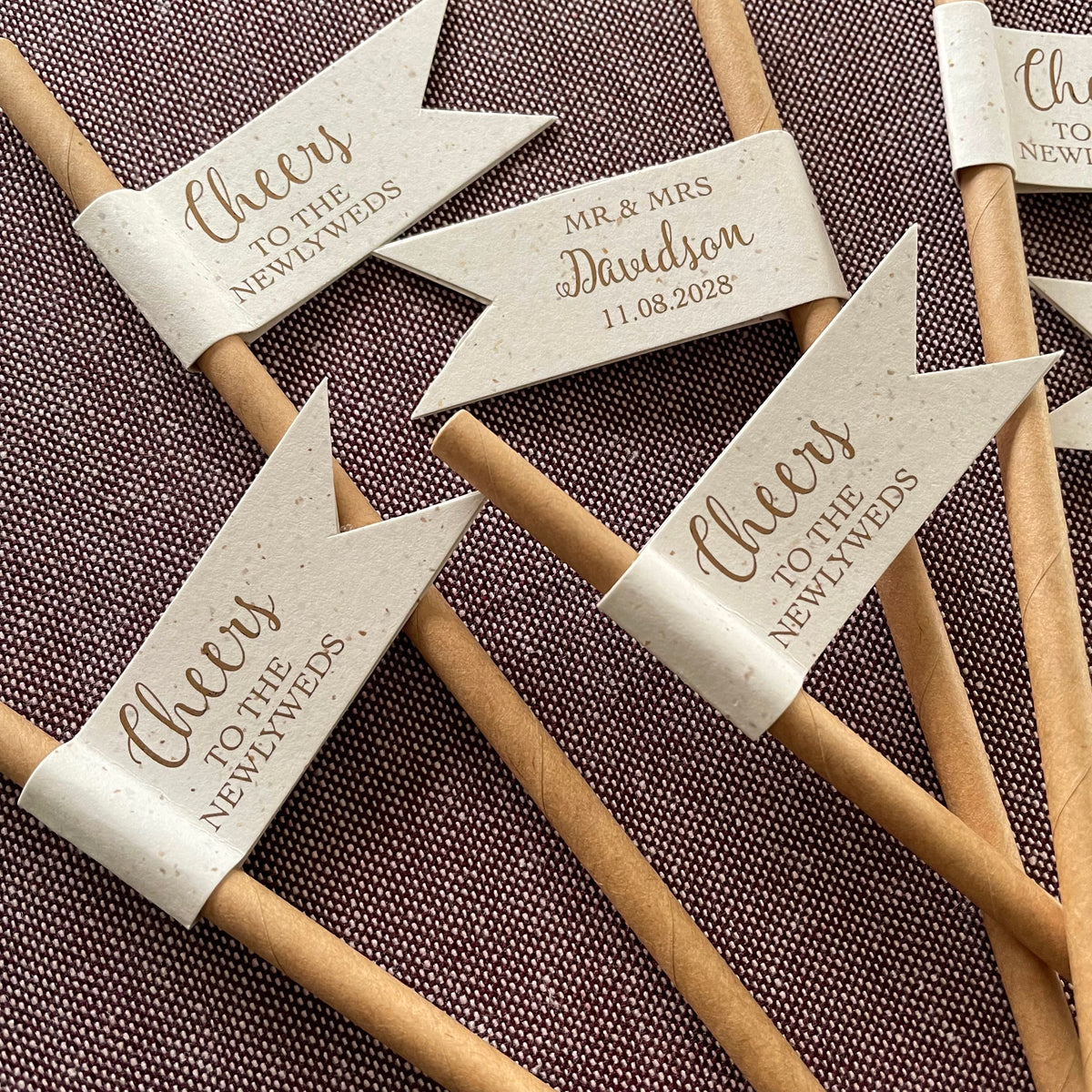 Decorative brown paper straws with recycled flag shape with bronze foil text cheers to the newlyweds on the front and customisable text on the back with couples married name and date. for wedding drinks on arrival