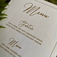 close up of wedding menu card in white and gold