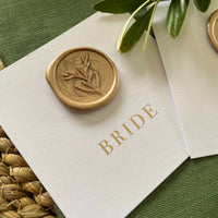 gold foil name cards on flat white card with gold wax seal foliage leaf design for place settings for wedding