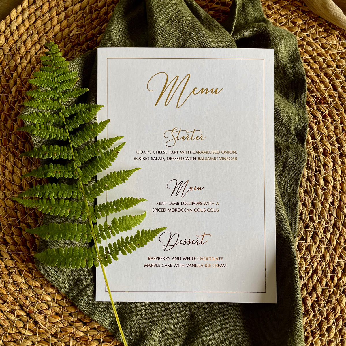 A rectangular white menu card with elegant gold script text with border for table settings
