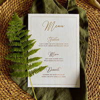 A rectangular white menu card with elegant gold script text with border for table settings