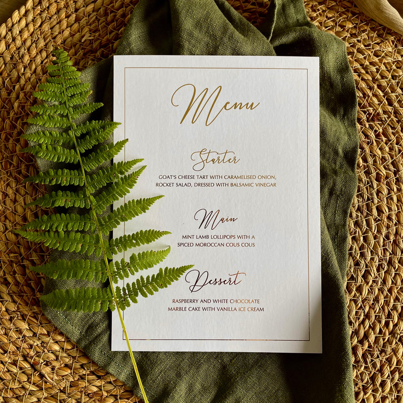 A rectangular white menu card with elegant gold script text with border for table settings